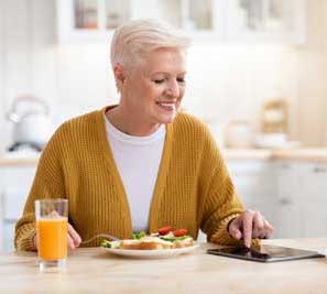 Senior eating healthy food at home while using tablet